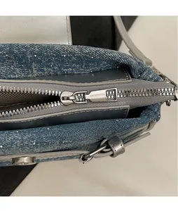 Detail of smooth silver hardware zipper pull on blue denim shoulder bag texture