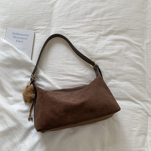 Macro shot of dark brown suede baguette bag with a plush bear charm on white fabric