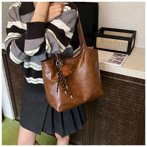 Detail of dark brown faux leather tote bag with teddy bear charm and fringe tassel