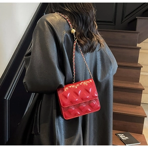Detalle de bolso bandolera rojo acolchado con cadena dorada llevado por una modelo