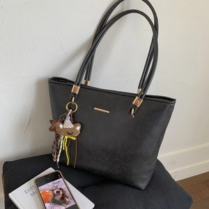 Detail view of black PU leather tote bag with gold metal trim and brown bear charm