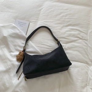 Detail of black suede bag with plush charm on white linen, minimalist vintage style