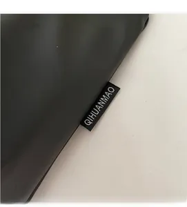 Detailed view of the QIHUANMAO brand label stitched on a black leather crossbody bag