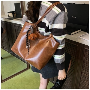Brown leather tote bag featuring a cute plush bear charm and spacious shoulder strap