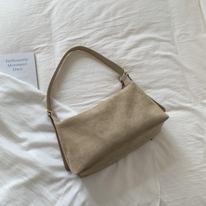 Detail view of camel suede baguette bag with smooth leather strap on white fabric
