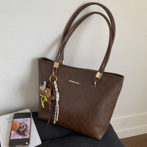Detail of dark brown PU leather tote bag with cute bear charm and woven tassel accent