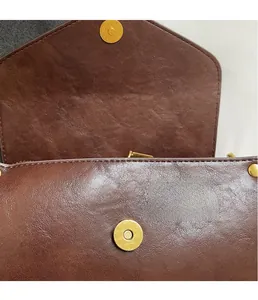 Detail of the high-quality gold magnetic buckle on a dark brown textured leather bag