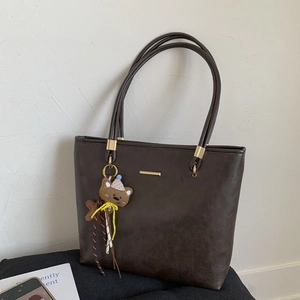 Detail of dark brown PU leather tote bag with gold metal trim and cute bear plush charm