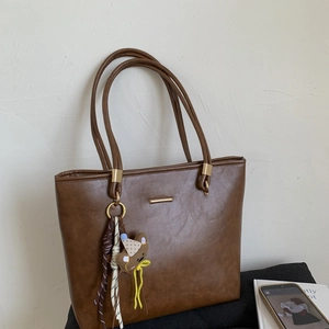 Detail of deep brown tote bag featuring gold hardware and a cute bear bag charm