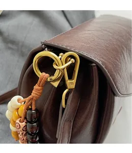 Close-up of golden hardware clasp and colorful beaded tassel on dark brown leather bag