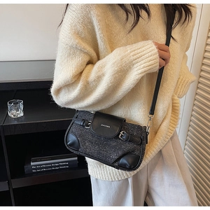 Detail of a dark grey tweed crossbody bag with leather trim worn with a beige sweater