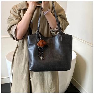 Detail shot of a dark coffee tote bag with a plush puppy charm on a model in a trench coat