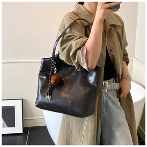 Detail view of large black leather tote bag with vintage texture and plush tassel charm