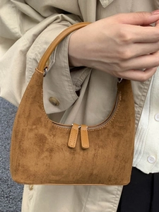 Chic caramel suede crescent hobo bag with leather handle held by model in trench coat