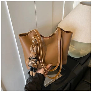 Detail of a brown leather tote bag featuring wave-edged opening and a cute bunny charm