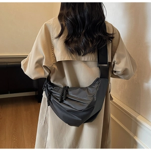 Detailed back view of a minimalist black crescent crossbody bag worn over a trench coat