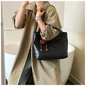 Detail of minimalist black leather tote bag featuring a cute brown plush bear charm