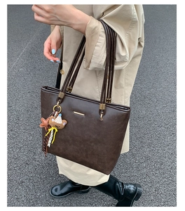 Detail view of large dark brown leather tote bag with star and bear charms on model