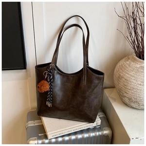 Detail of dark brown leather tote bag with vintage texture and plush bear charm