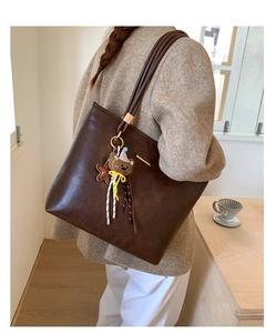 Detail of dark brown vintage tote bag with a cute bear charm and tassel on the strap