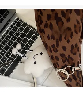 Cute white plush cloud keychain with smile face detail hanging on a leopard print tote bag