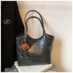 Detail of black PU leather tote with brand logo and cute brown teddy bear keychain
