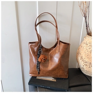 Close-up of brown textured leather tote with a cute plush puppy and fringe charms