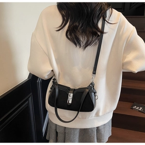 Detail view of black matte leather shoulder bag with silver buckle worn by a model