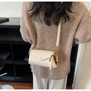 Detail of a creamy white crossbody bag with envelope flap and colorful wooden beads charm