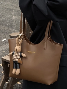 Brown leather tote bag with elegant bunny charm and golden fashion text on outdoor background