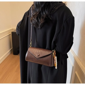 Detail view of a vintage brown leather crossbody bag with ethnic beaded charm and gold hardware
