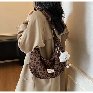 Close-up of leopard print canvas crescent bag with a white plush cloud charm and logo tag