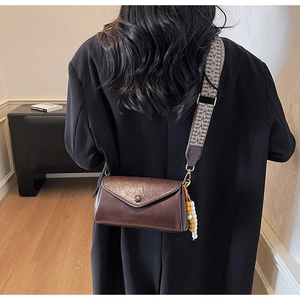 Detail view of brown crossbody bag with ethnic patterned strap and beaded tassel decor