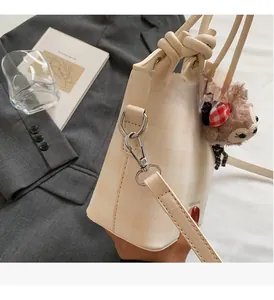Detailed view of cream checkered bucket bag with silver hardware and plush pendant
