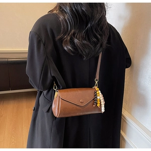 Detail of a brown leather envelope bag featuring natural beaded tassels on the side