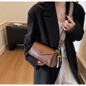 Detail of a brown leather crossbody bag with ethnic woven strap and wooden beads decoration