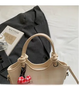 Detail of beige quilted handbag with red plaid bow charm and knotted handle design
