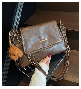 Detail of vintage brown tote bag texture with gold bar trim and plush bear charm on wood