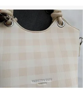 Close-up of beige checkerboard pattern handbag with silver fashion logo and knotted handle