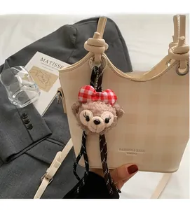 Detail of beige checkered bucket handbag with a plush bear charm on fashion magazine