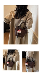 Detail view of dark brown checkerboard bucket bag with plush bear charm and long strap