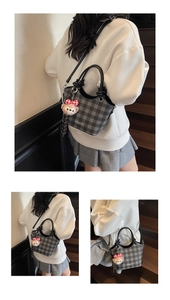 Detail of grey checkered handbag featuring white fashion text and a plush toy charm