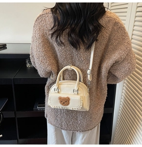 Detailed view of cream crossbody bag with bear patch and ruffled trim on a model