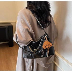 Detail view of black faux leather tote bag with metal chain strap and teddy bear charm