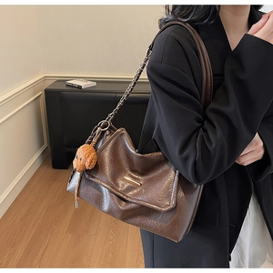 Detail of dark brown leather tote with gold bar, chain strap and teddy bear charm