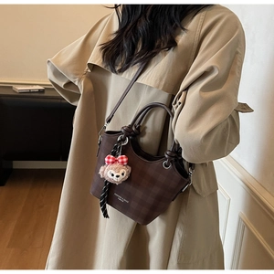 Detail view of the brown checkerboard tote bag with pink fox charm and shoulder strap