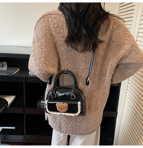 Detail of a black mini handbag featuring a brown bear patch and white lace trim detail