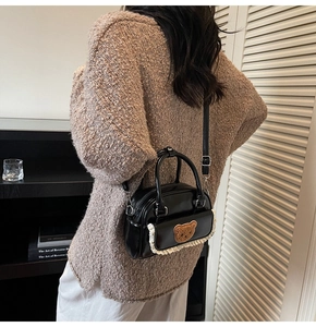 Detail of black glossy handbag with teddy bear patch and lace trim on crossbody strap