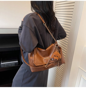 Detail of brown leather tote bag with gold chain strap and teddy dog plush pendant