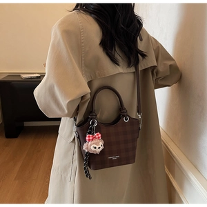 Detail of dark brown checkered crossbody bag with plush bear charm on beige trench coat